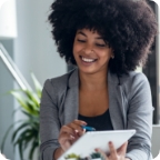 Business woman smiles while pointing to a tablet.